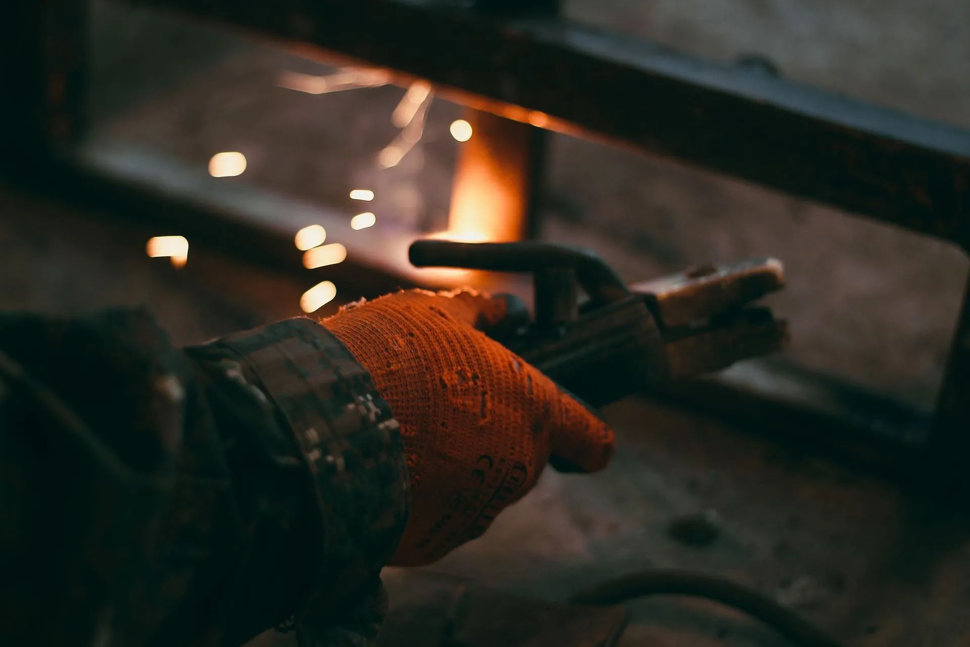 A welder's gloved hand holding an electrode rod clamped in the holder